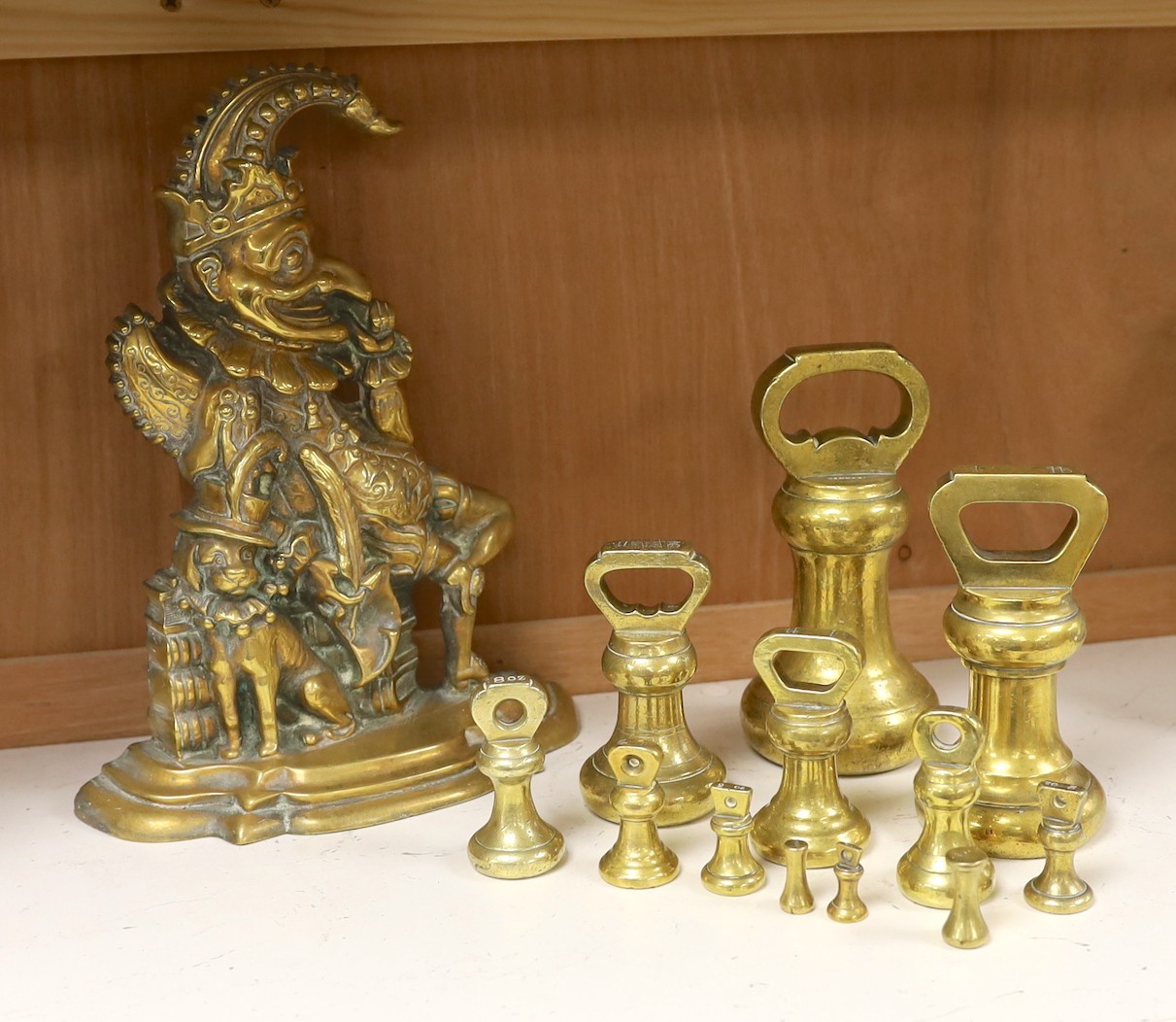 A graduated set of twelve brass bell weights and a cast brass “Punch’’ door stop. 30cm